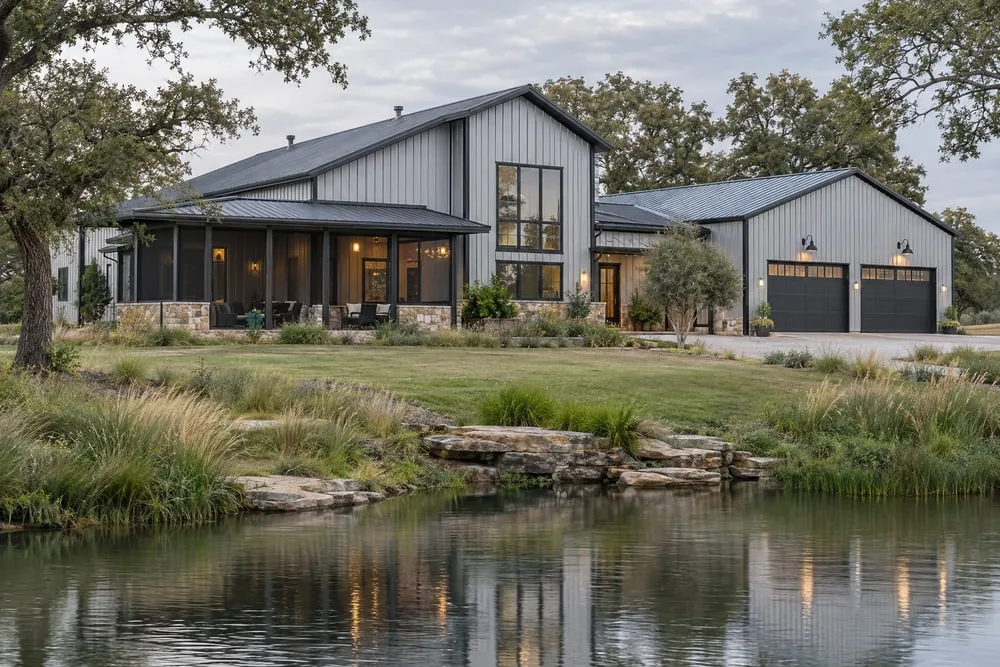 Grey steel barndominium home with a screened porch and two-car garage beside a pond